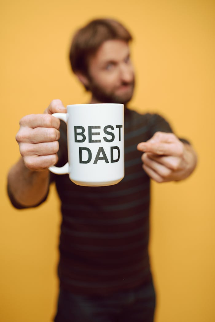 Man presenting a mug with Best Dad text against a warm yellow background.
