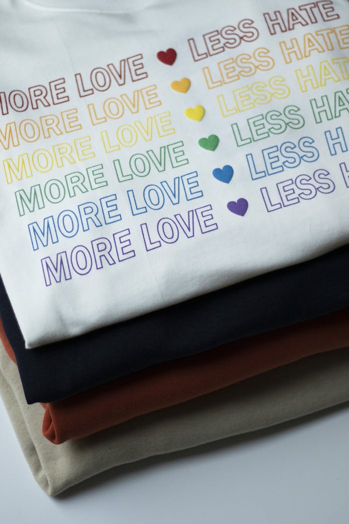 Stack of rainbow-themed shirts with More Love, Less Hate message.